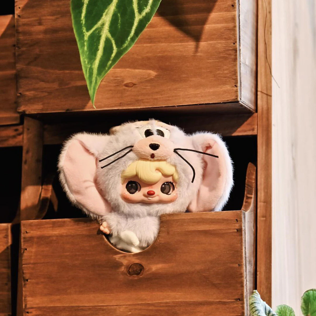 POUKAPOUKA in a white Tom costume peeking from a wooden cubby