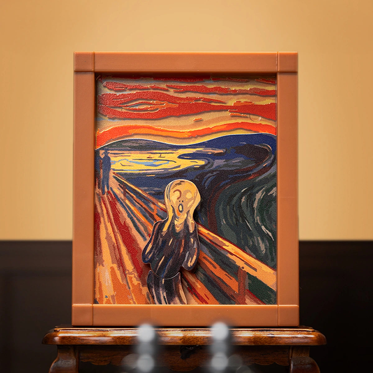 The Scream skull-faced figure in orange frame on a wooden table, QueSera Living Paintings wind-up diorama