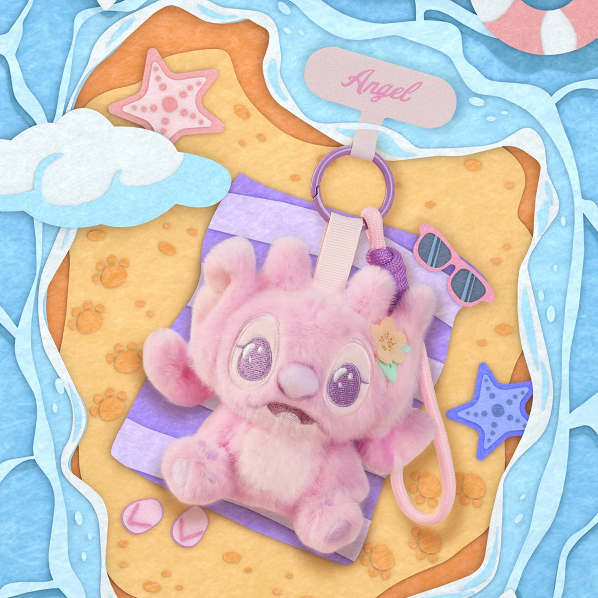 Angel plush phone strap reclining on a beach towel beside sunglasses and starfish