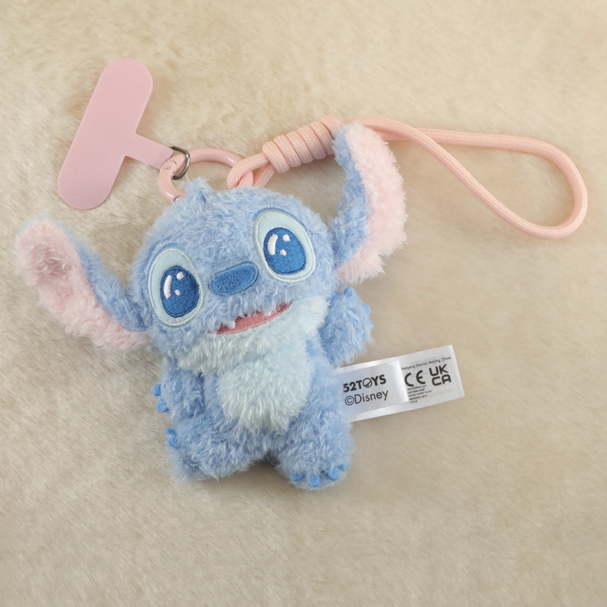 Wide-eyed Stitch plush phone charm lying on a cream fabric background