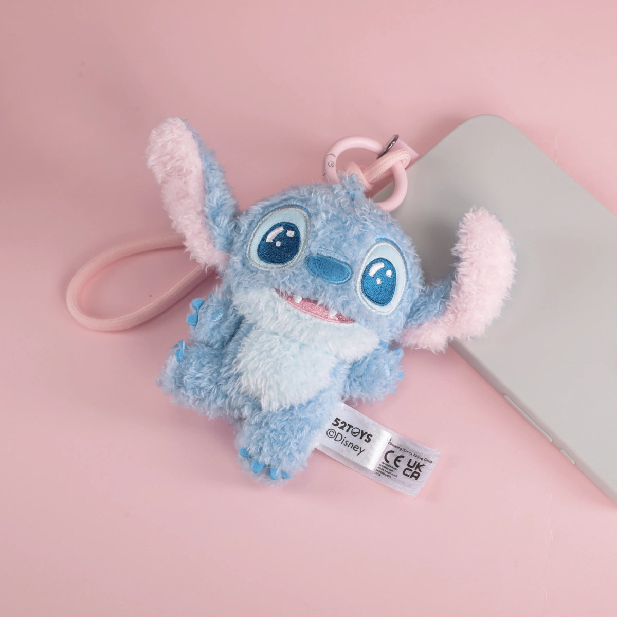 Excited Stitch plush phone charm with both ears raised on a pink background